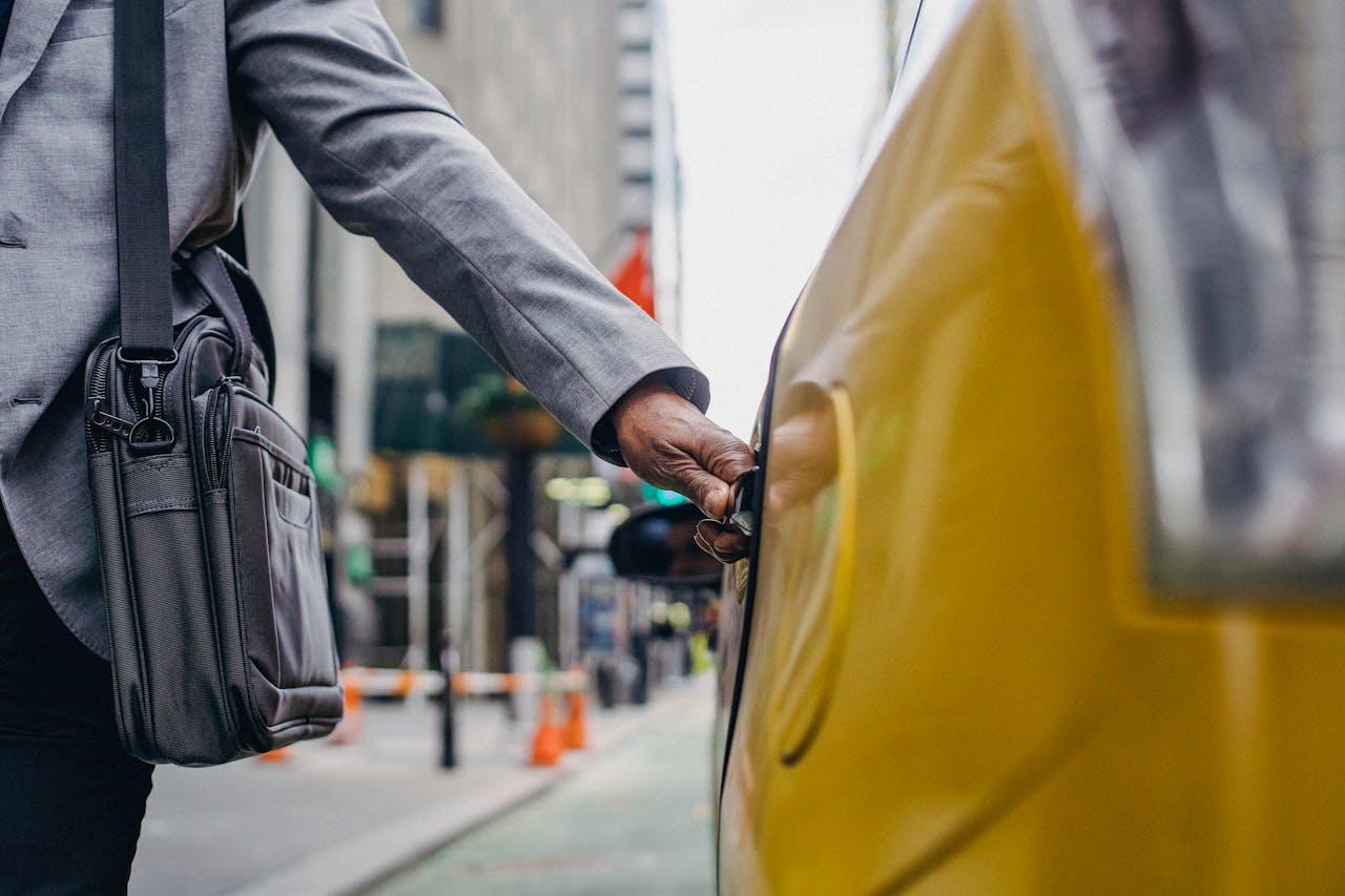 A businessman in a suit opens a yellow taxi door in an urban setting, highlighting travel and commute.